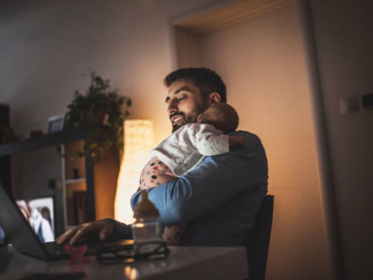 Man working on laptop with baby sleeping on his chest